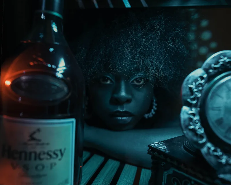 Low-key portrait beside a cognac bottle, lit in deep teal